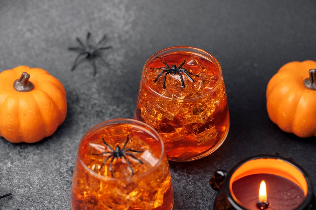 Two spooky Halloween drinks with spiders and mini pumpkins on dark background